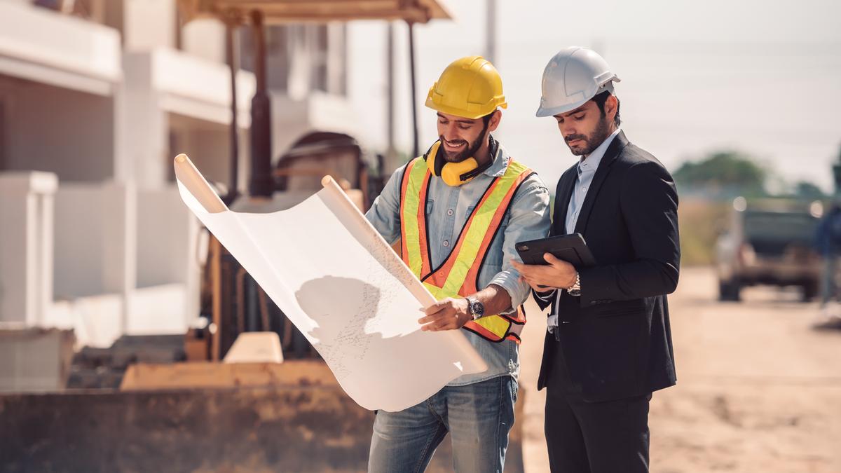 A field supervisor and site engineer reviewing plans on a tablet at a construction site