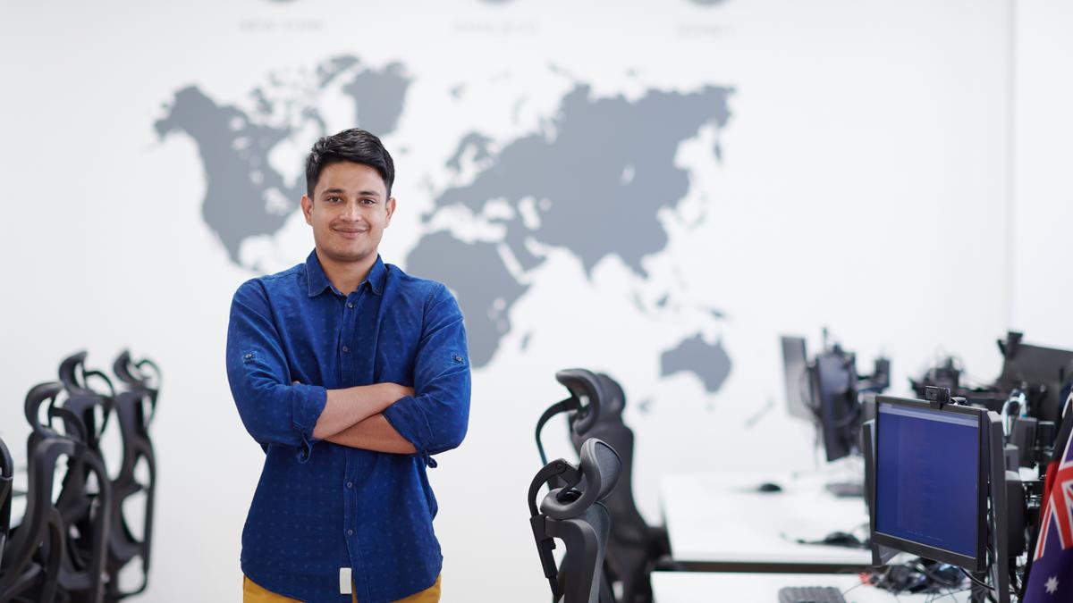 A confident employee standing in a global office in front of a world map, representing multi-entity org structure